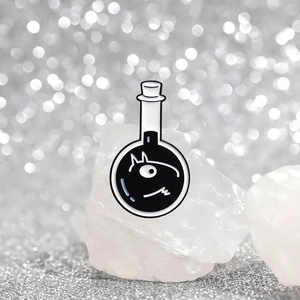 Macro detail of cartoon cat enamel pin in flask shape on decorative white crystals