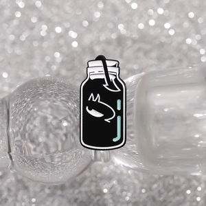 Macro shot of a black and white enamel cat pin shaped like a bottle on a glittery background