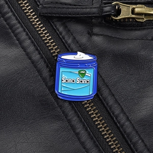 Close-up of Sana Sana blue cream jar enamel pin on a black leather jacket texture