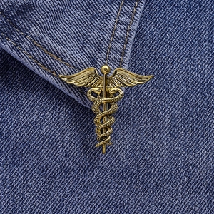 Detailed close-up of a gold caduceus medical brooch pinned on blue denim fabric texture