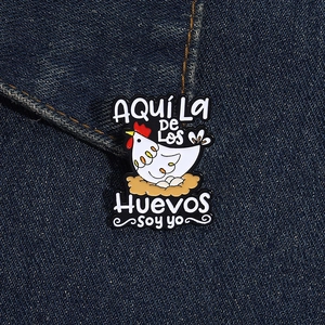 Detailed close-up of a white hen enamel pin with Spanish text on denim fabric