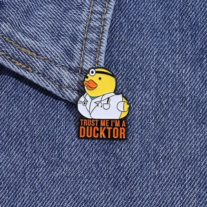 Dettaglio di una spilla in smalto a forma di papera dottore con scritta Trust Me I am a Ducktor