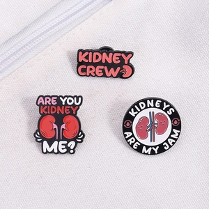 Detailed view of three creative enamel pins featuring cartoon kidney designs on white fabric