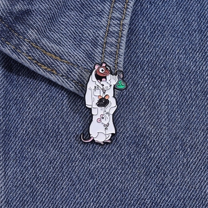 Detail of three mice in lab coat enamel pin on blue denim fabric background