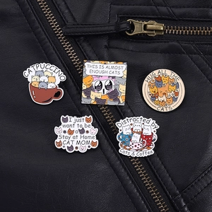 Detail of five cute cat enamel pins on a black leather jacket featuring funny cat slogans