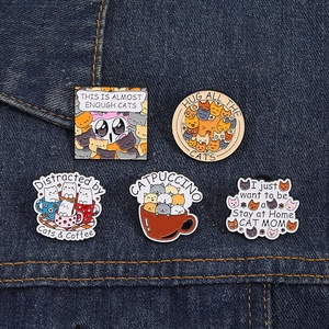 Detail of five cute cat enamel pins featuring cartoon designs on denim fabric