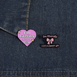Detail of pink heart and bow enamel pins with trendy slogans on denim fabric
