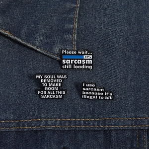Nahaufnahme von drei schwarzen Emaille-Pins mit Ladebalken-Sarkasmus auf Denim-Stoff