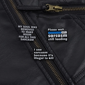 Detailansicht von drei schwarzen Emaille-Sarkasmus-Pins an einer schwarzen Lederjacke