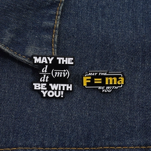 Detailed close-up of two physics theme enamel pins showing F=ma formula on denim fabric