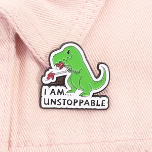 Dettaglio della spilla in smalto a forma di dinosauro verde con slogan I Am Unstoppable