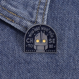Detail of Iron Giant enamel pin with movie quote on blue denim fabric background