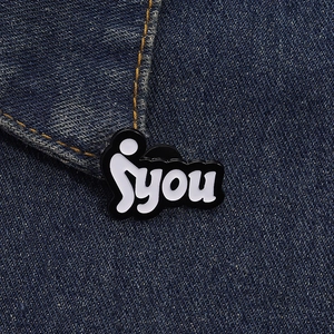 Close-up of a creative black and white enamel YOU brooch pinned on blue denim fabric