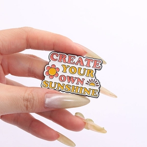 Dettaglio spilla 'CREATE YOUR OWN SUNSHINE' con disegni di fiori e sole colorati