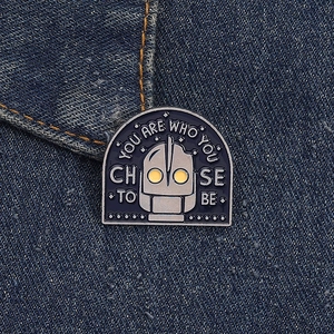 Close-up of Iron Giant enamel pin with quote on dark blue denim fabric background