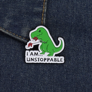 Dettaglio spilla smaltata dinosauro verde su denim con scritta motivante Unstoppable