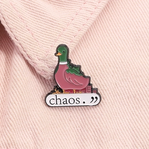 Detail of cute green duck enamel pin with chaos slogan on pink denim jacket texture