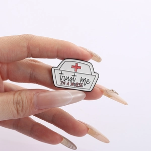 Detail of nurse cap enamel pin with Trust me I'M A NURSE text held in hand for scale