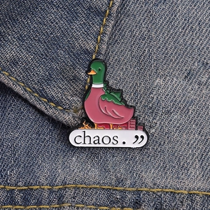 Detail of chaos duck enamel pin with green spikes and burning city on denim fabric