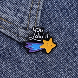 Macro shot of cartoon shooting star enamel pin with 'you did it' text on denim fabric