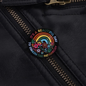 Detail of round enamel pin with rainbow and text on black leather jacket