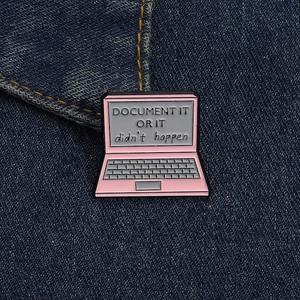 Detail of pink laptop enamel pin with Document It Or It Didn't Happen text on denim