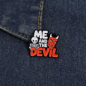 Close-up of enamel skull and devil badge pinned on blue denim with Me and the Devil text