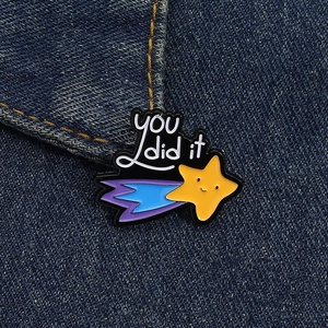 Detail of a shooting star enamel pin with 'you did it' text on denim fabric