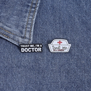 Detailed macro view of trust me I am a doctor and nurse enamel pins on denim