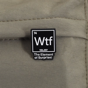 Vue macro d'un pin's carré en émail avec l'élément chimique Wtf sur un tissu vert