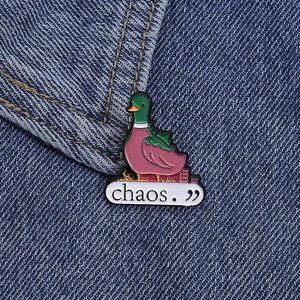 Detail of cute green duck enamel pin with 'chaos.' text on blue denim fabric background