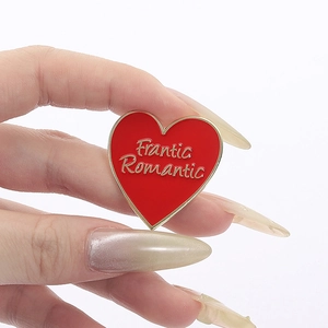 Macro shot of a red heart enamel pin featuring golden Frantic Romantic lettering detail