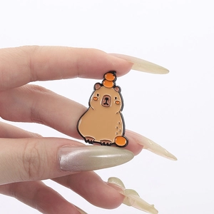 Détail d'une mignonne épingle en émail Capybara tenue à la main sur un fond blanc neutre