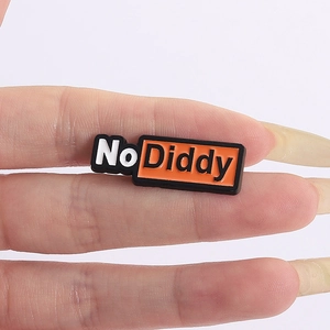 Gros plan d'un badge émaillé No Diddy avec design noir et orange tenu entre les doigts