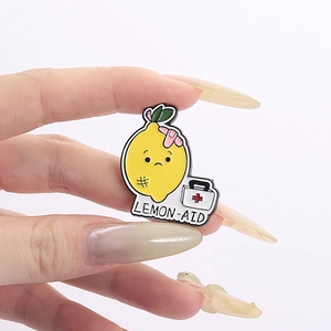 Détail du pin's en émail citron triste Lemon-aid tenu à la main sur un fond blanc neutre