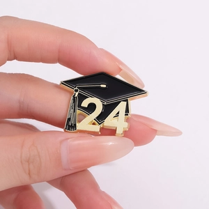 Detailed view of hand holding a 2024 graduation cap enamel pin with golden tassel