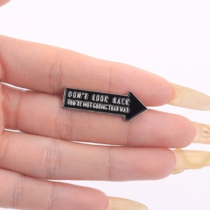 Detail of black arrow enamel pin with white Don't Look Back quote held in hand
