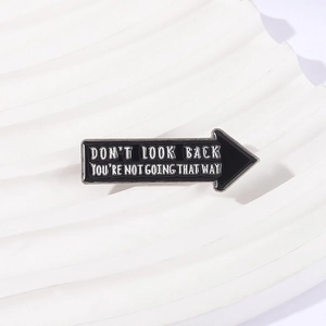 Black enamel arrow brooch with Don't Look Back quote on a textured white display