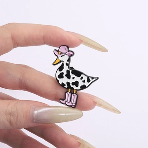 Close-up of duck enamel pin with black and white cow patterns and pink cowboy hat