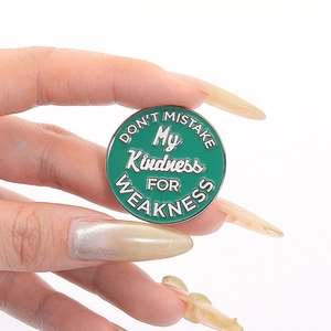 Macro shot of green enamel brooch with Don't Mistake My Kindness for Weakness quote
