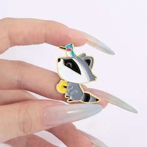 Détail d'un pin's en émail raton laveur avec oiseau bleu présenté sur une main