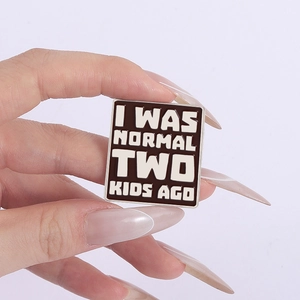 Close-up of square enamel pin with I WAS NORMAL TWO KIDS AGO funny quote engraving