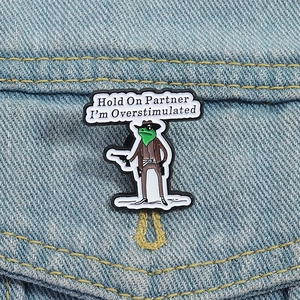 Cowboy frog enamel pin with Overstimulated text on blue denim jacket pocket