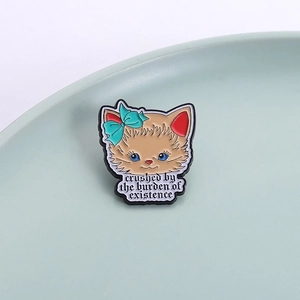 Cute ginger cat enamel pin with a teal bow and artistic text on a high-quality metal badge