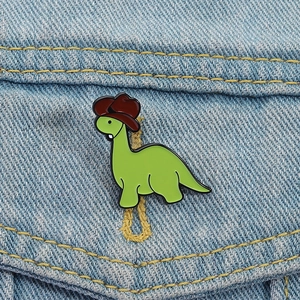 Épingle émaillée dinosaure vert avec chapeau de cow-boy sur veste en jean bleue