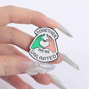 Detail of enamel pin with hands forming a heart and Together We Are Unlimited text