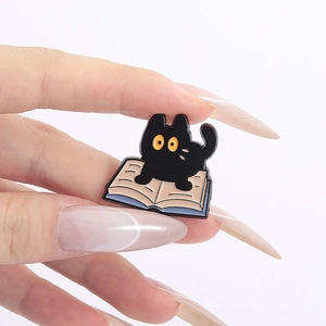 Detailed view of an enamel pin featuring a black cat resting on an open book