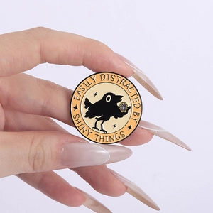 Detailed enamel pin showing a black raven holding a shiny purple gem with funny text