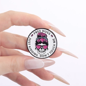 Detail of hand holding a pink skull enamel badge with Free Hugs engraving
