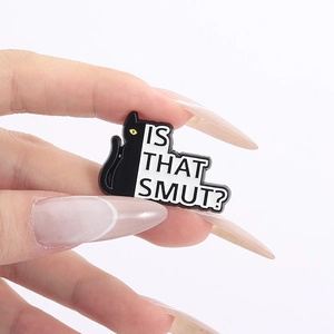 Detail of a black cat enamel pin with yellow eyes and 'IS THAT SMUT?' speech bubble text